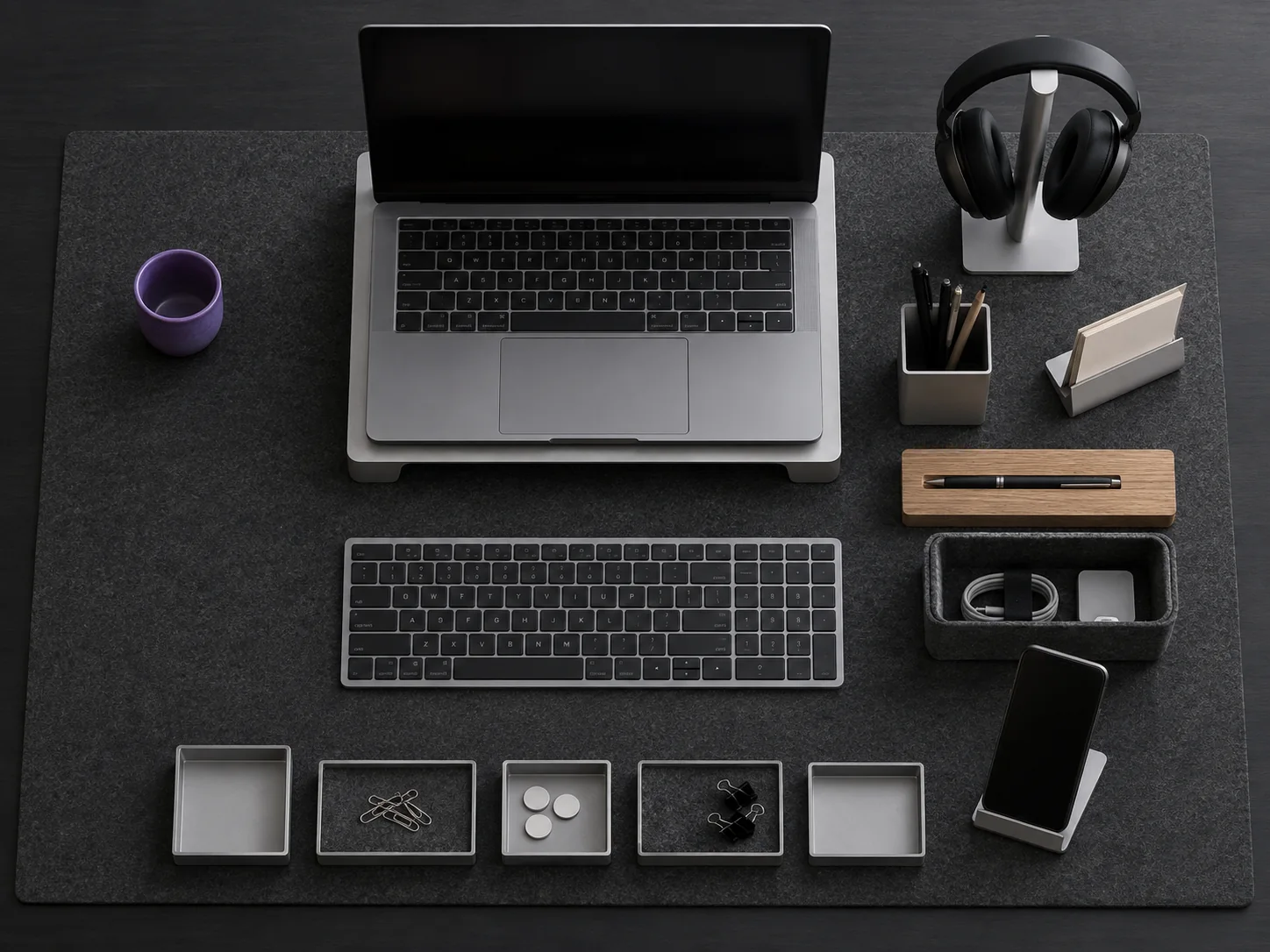 Aufsicht auf einen Schreibtisch mit IRIDAVO-Modulen: Laptop-Ständer, Ablagen, Stiftebecher, Eichen-Stifteblock, Filz-Behälter, Smartphone-Ständer und Kopfhörer-Ständer auf einer Filz-Schreibtischunterlage.